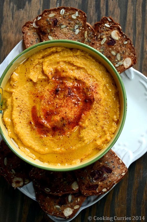pumpkin hummus in a bowl with some crackers on a plate on the side
