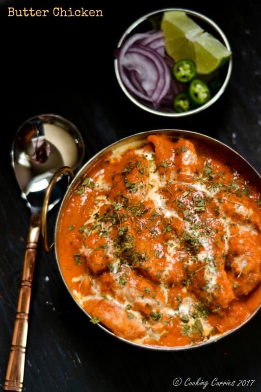 Butter Chicken in a kadhai with a small bowl of onion slices and lime wedges next to it