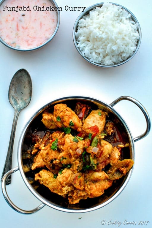Chicken Curry in a kadhai style pan with a spoon on the side