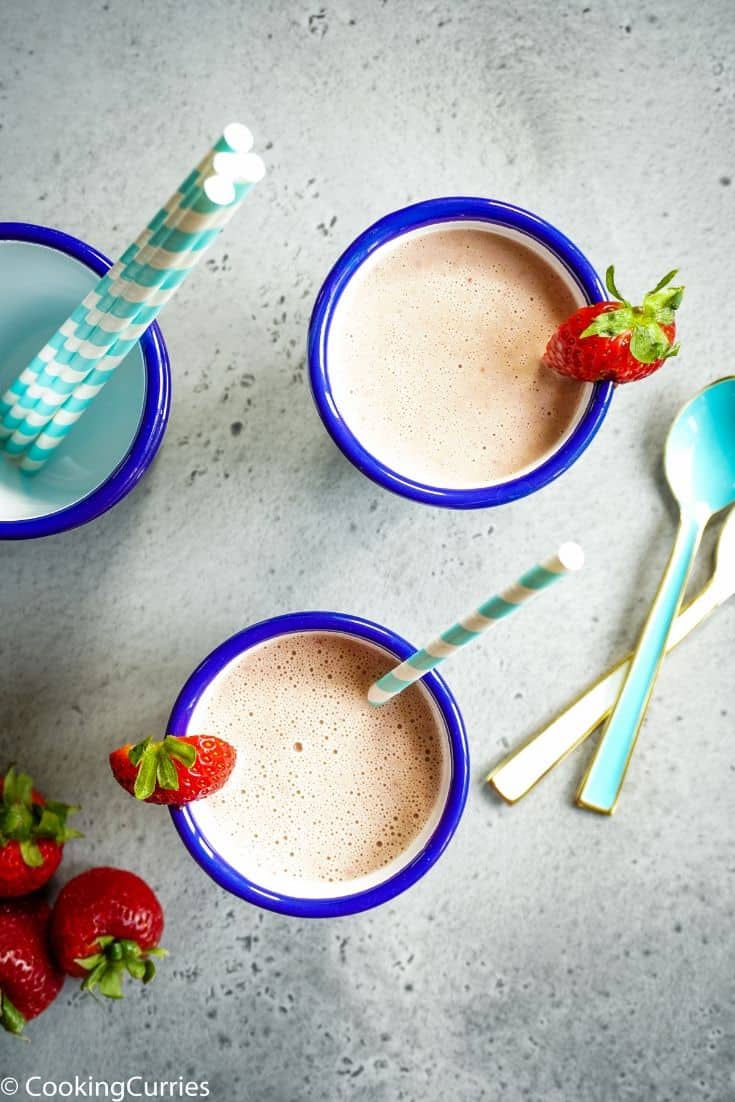PBJ smoothie in two white metal glasses with blue rim with a strawberry on top