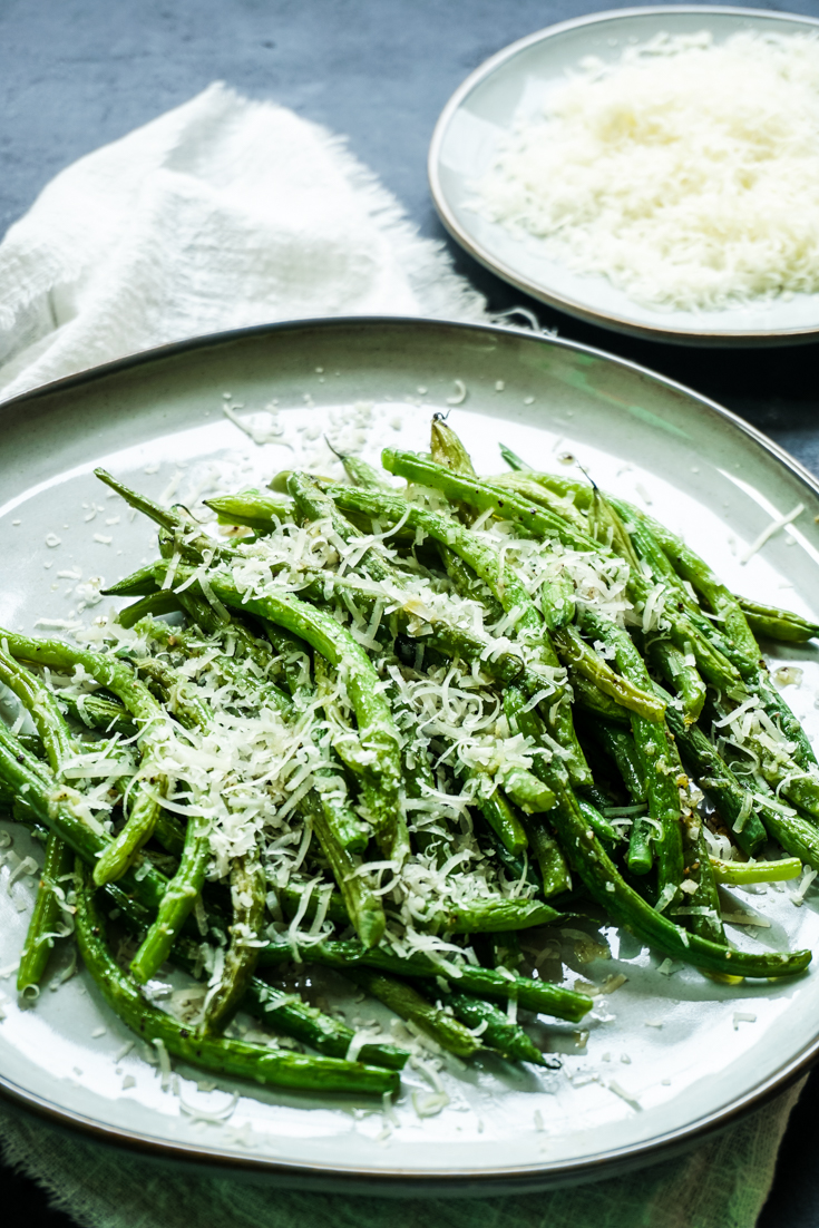 Side shot of green beans piled on a plate with grated parmesan on top