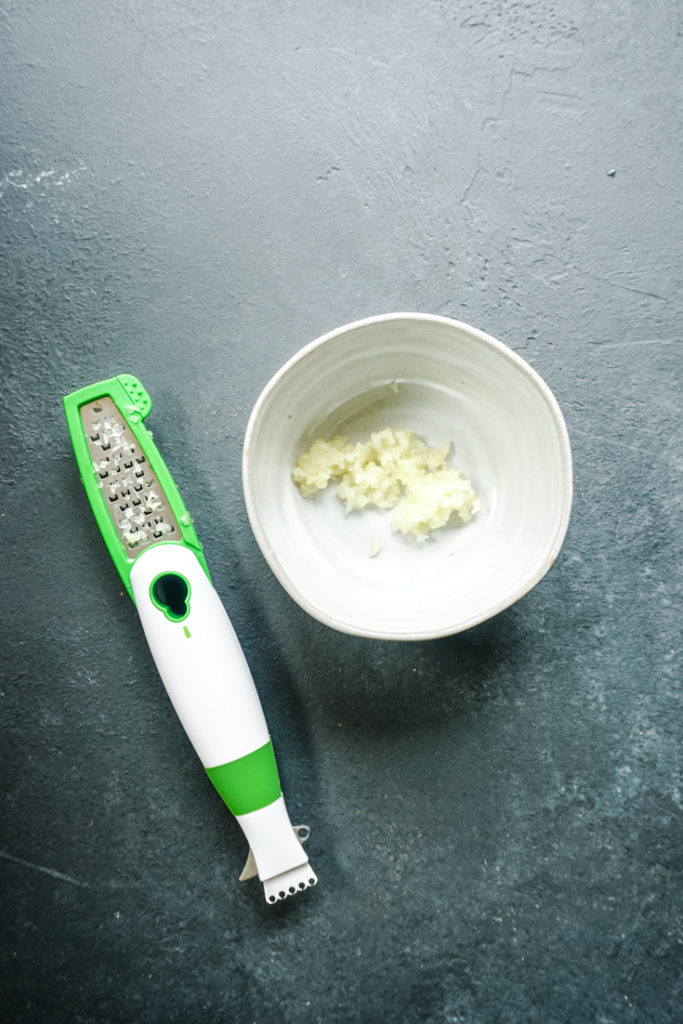 finely grated garlic in a white ramekin with the grater on the side