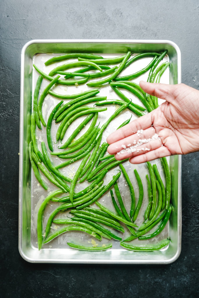 Coarse salt in palm of hand over a sheet pan of green beans