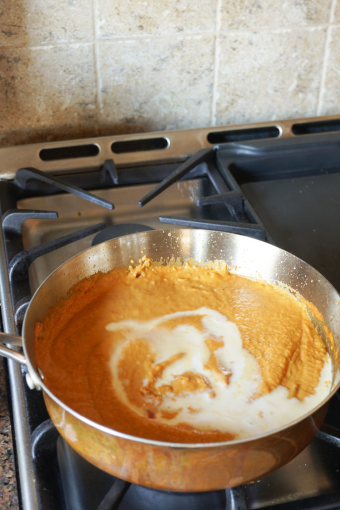 Stainless steel sauce pan on stove with sauce in it and some milk on top