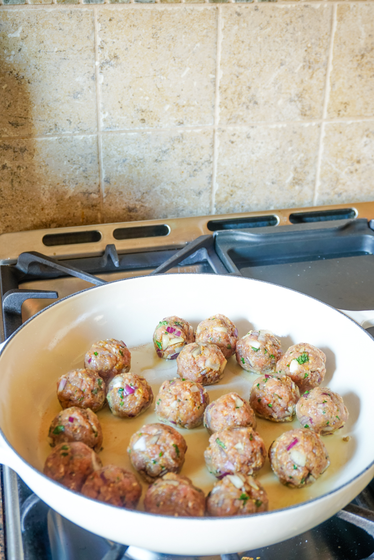 Meatballs cooking in a white cast iron pan on the stove