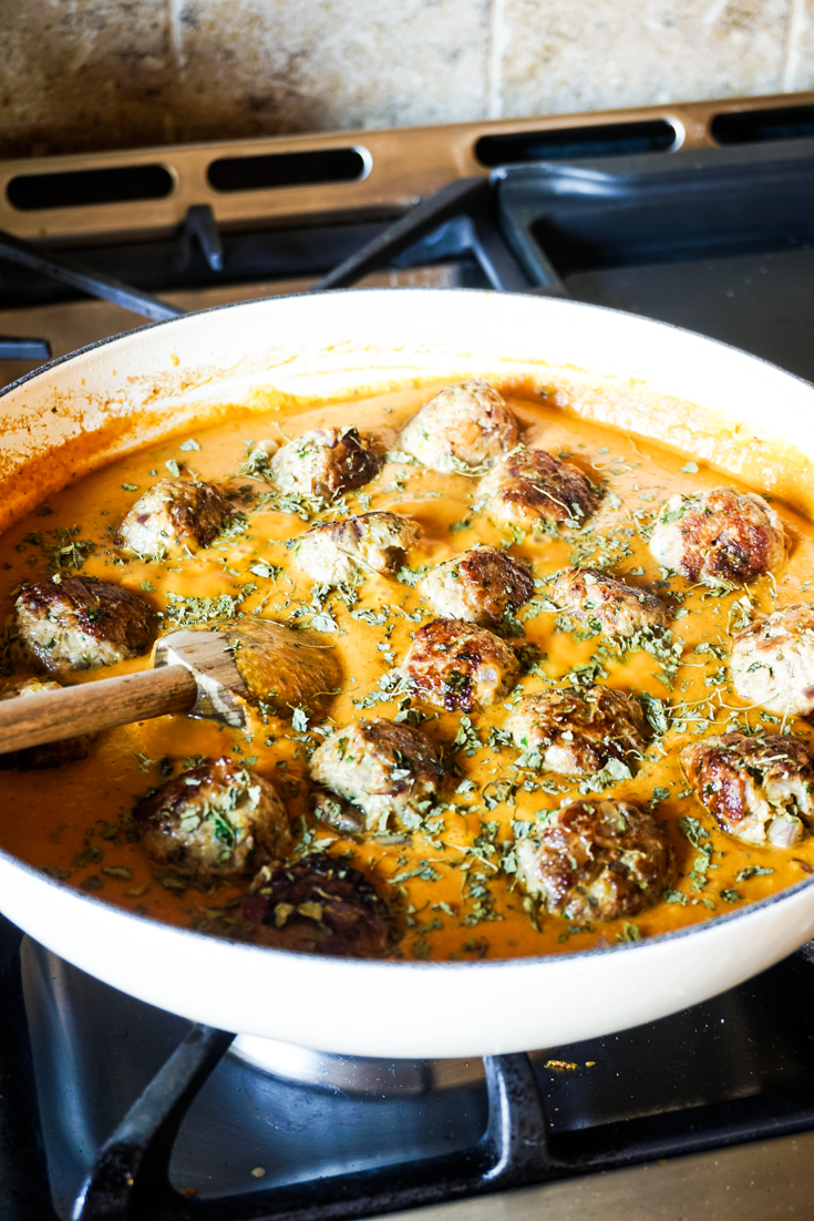 White cast iron pan on a stove with meatballs and sauce in it
