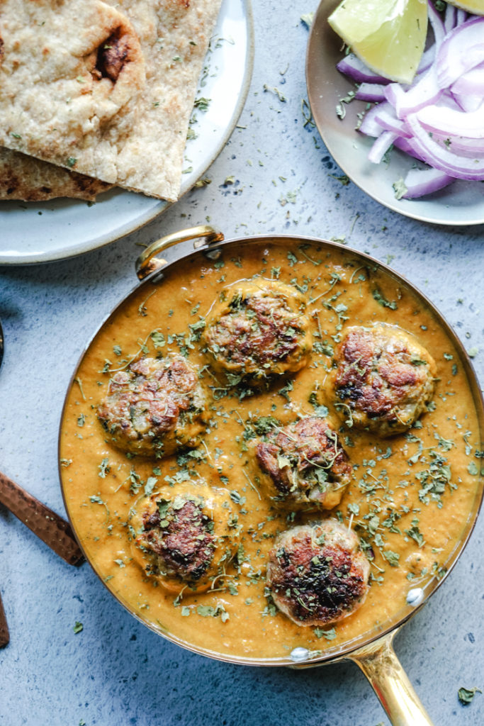 Meatballs in a creamy sauce in a serving pan with naan on the side