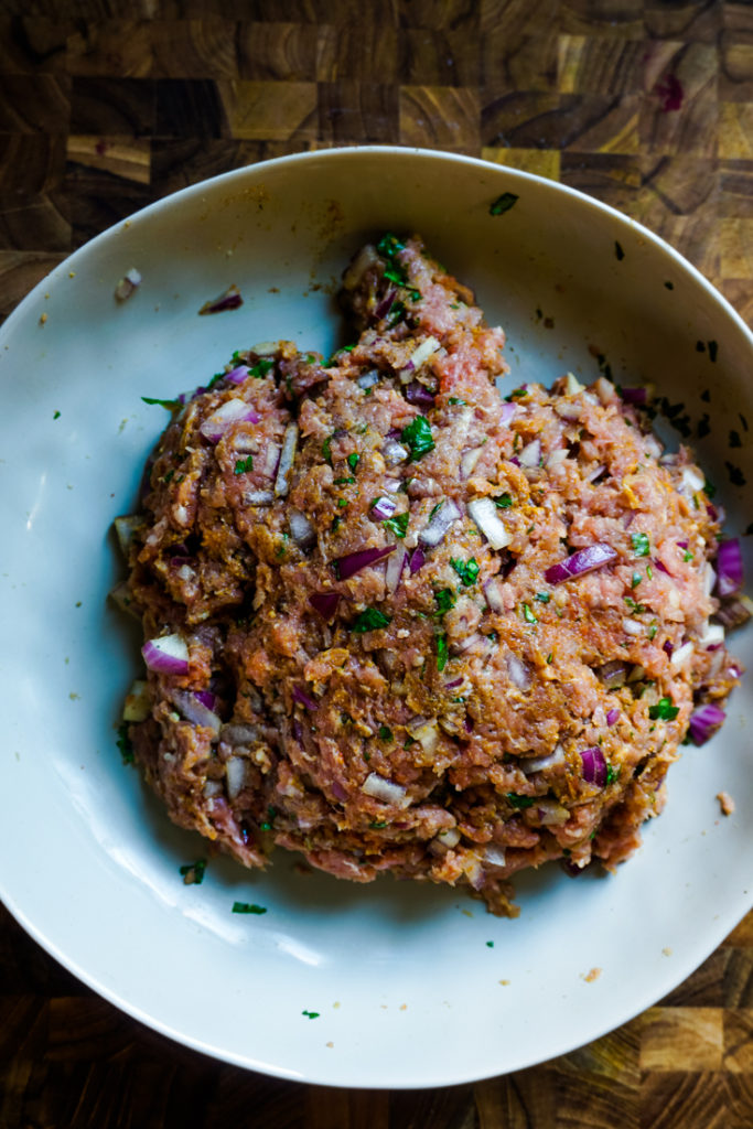 Ground turkey mixed with all the herbs and spices in a white bowl