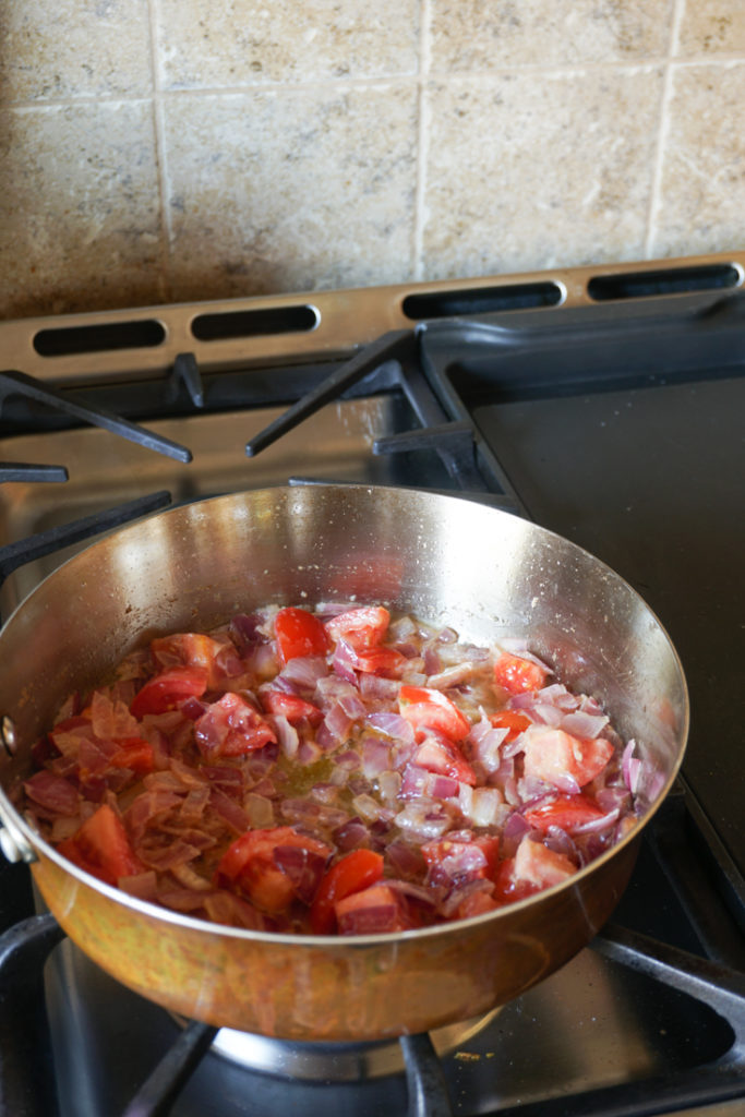 Onion and tomatoes sauteing in a steel pan on the stove