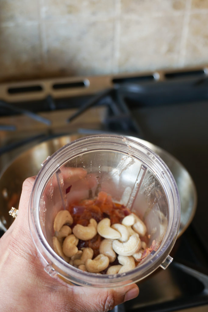 Blender jar with ingredients to be blended to a paste with cashew on top