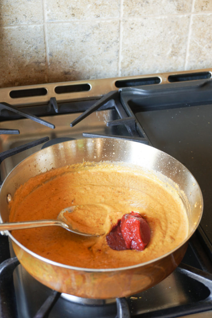 Stainless steel sauce pan on stove with sauce and tomato paste on top of it