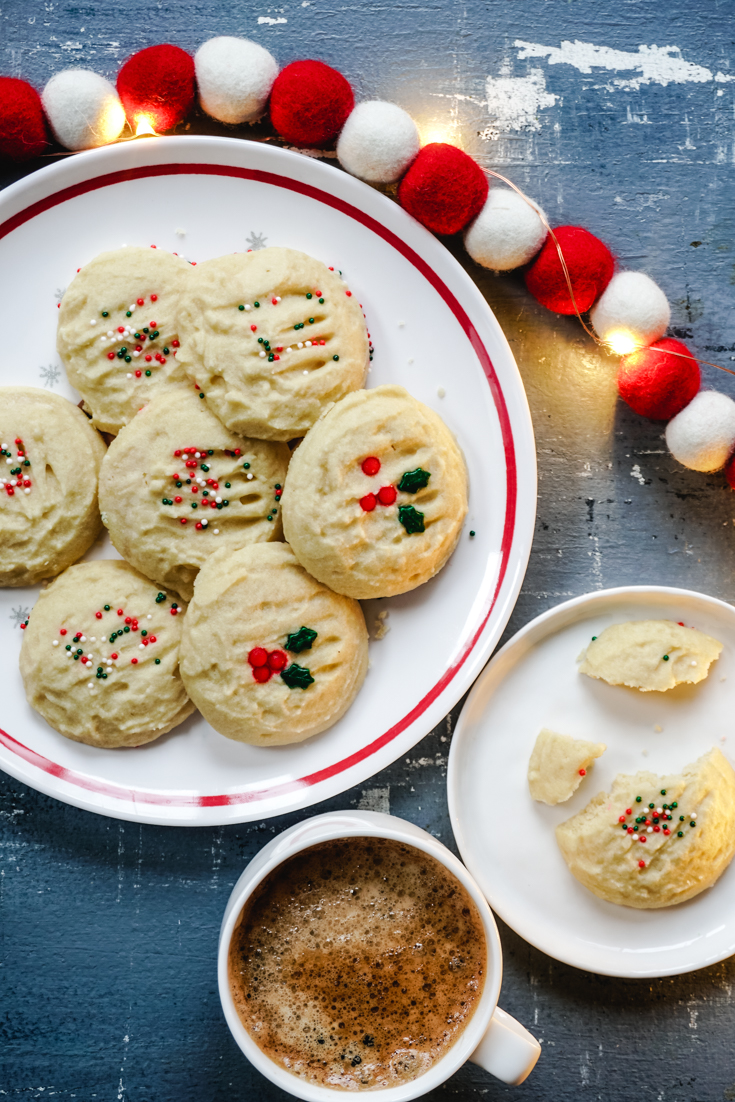 Cookies on a white plate with red rimwith a cup of coffee on the side of the plate