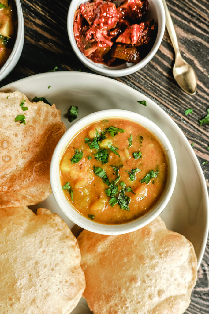 Platter with a bowl of potato curry and three pooris on the side