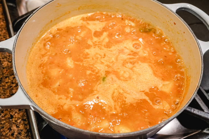 In process shot of potato curry bubbling in a large white pot