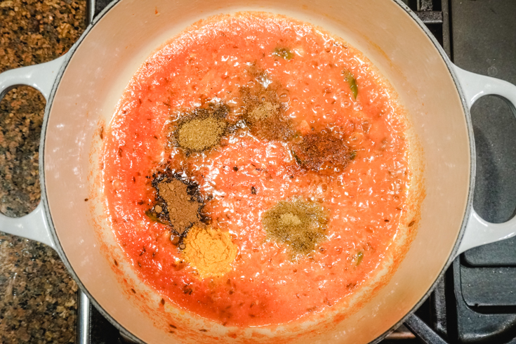 In process shot with spices in top of tomato sauce in a large white pot