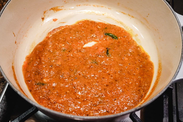 In process shot of thich tomato sauce cooking in a large white pot