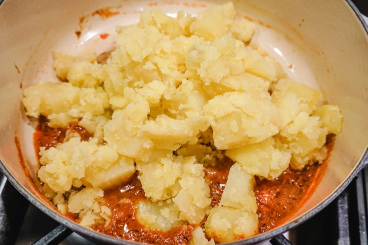 In process shot of crumbled potatoes on top of tomato sauce in a large pot