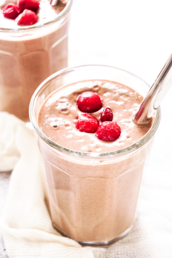 Angle shot of chocolate cherry smoothie in a glass with a stainless steel straw in it