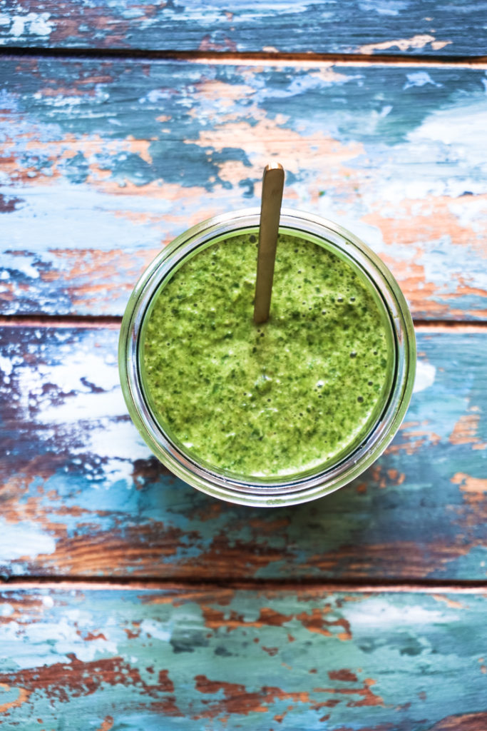 Top shot of cilantro mint chutney in a glass jar with a gold spoon in it