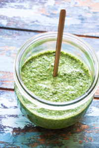 Angle shot of cilantro mint chutney in a glass jar with gold spoon sticking out