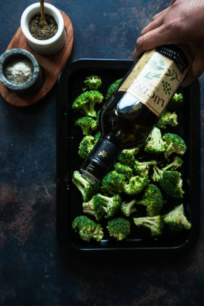Drizzling olive oil over broccoli in a black sheet pan