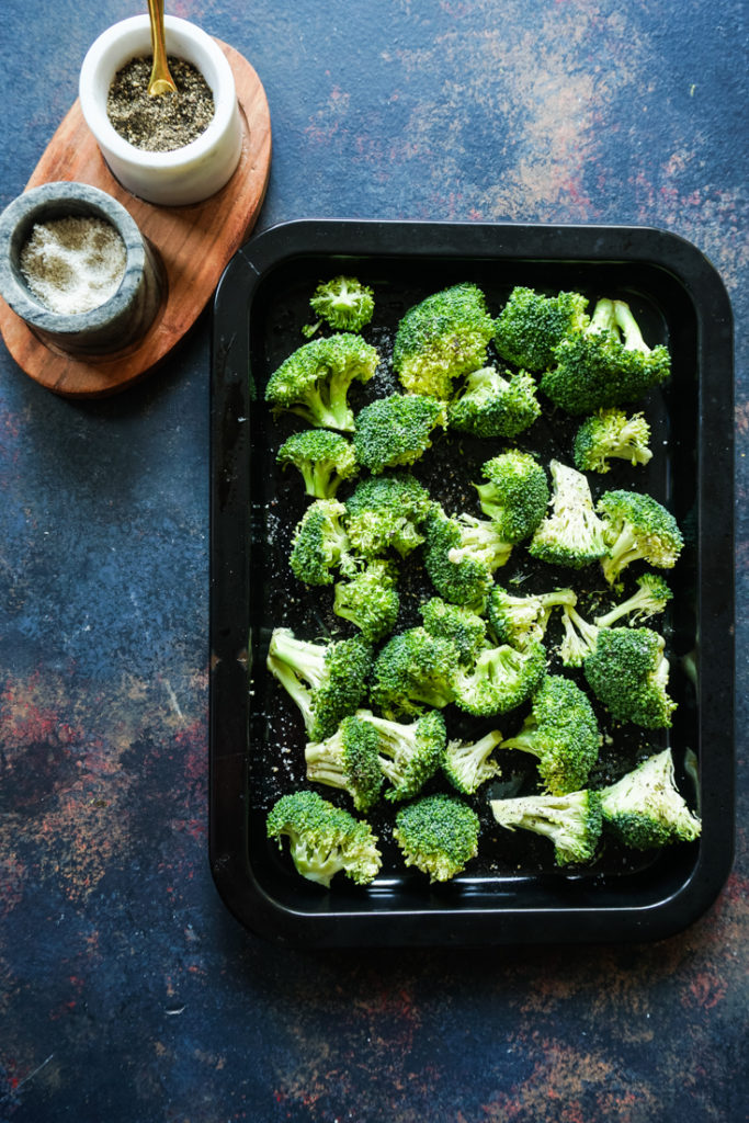 A black sheet pan with broccoli florets in it and a salt and pepper crock next to the sheet pan