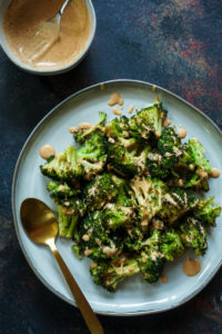 Top shot of Roasted Broccoli on a grey plate and drizzled with tandoori ranch on top, gold spoon on side of the plate
