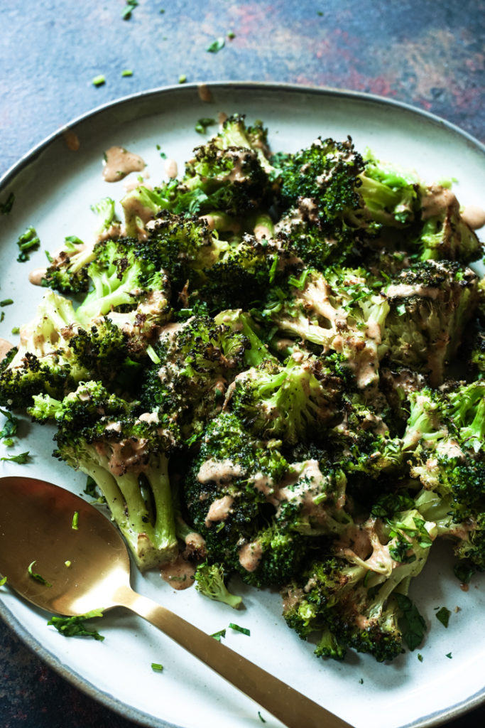 Roasted Broccoli on a grey plate and drizzled with tandoori ranch on top with a gold sppon on the side