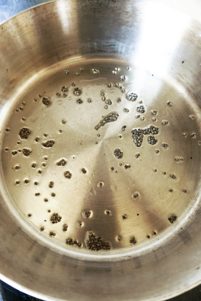 Oil in a pan stainless steel pan with brown mustard seeds in it