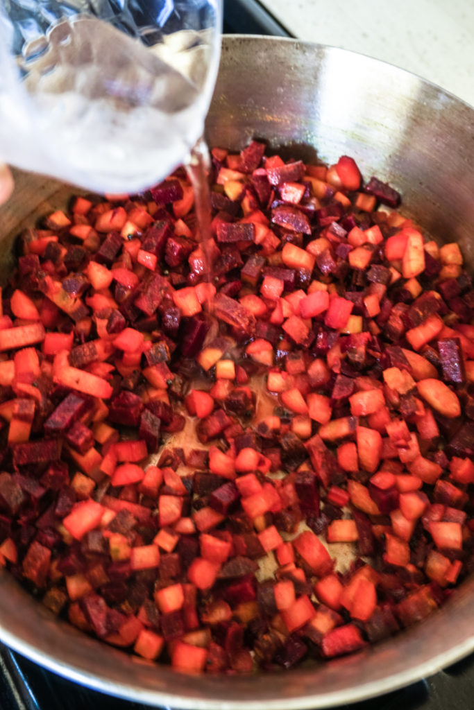 Water being poured into a pan with chopped beets and carrots in it