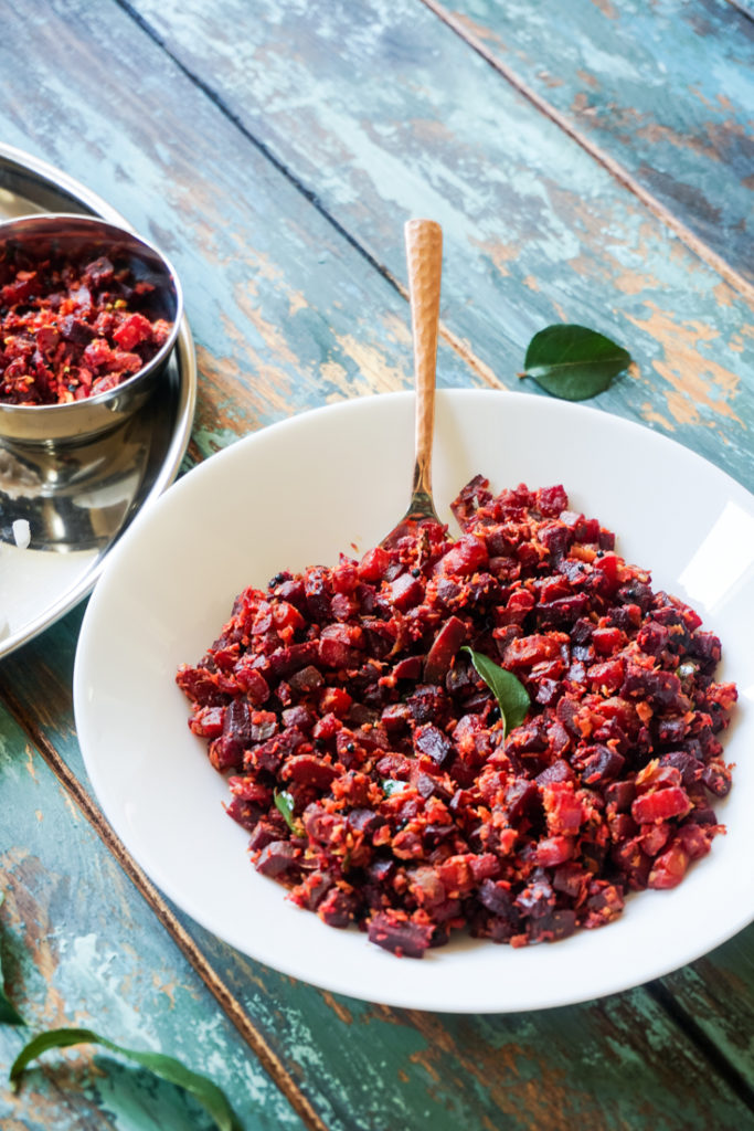 Angle shot of a white bowl with carrot and beets saute in it and a brass spoon sticking out