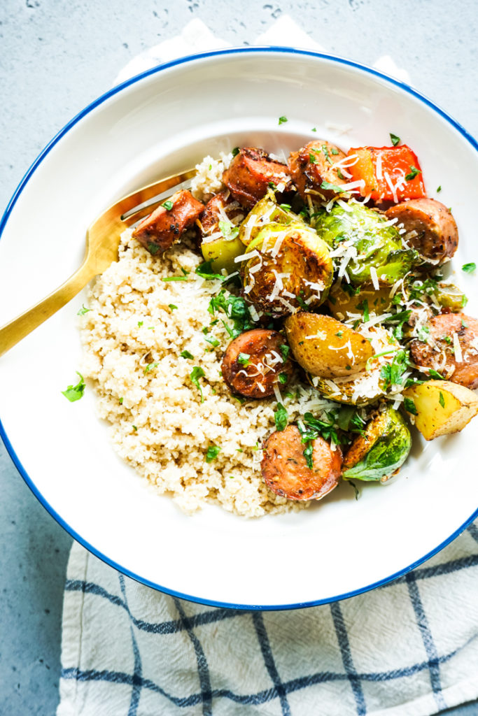 Sheet pan sausage and vegetables in a white bowl over some couscous