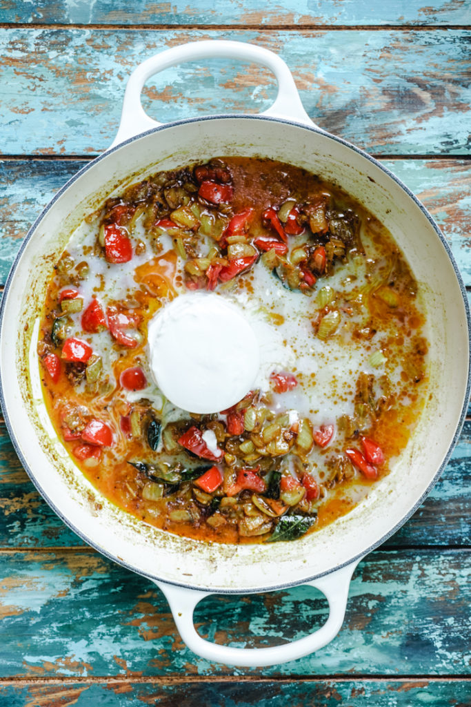Coconut milk added to cooked onions and tomatoes in a white dutch oven