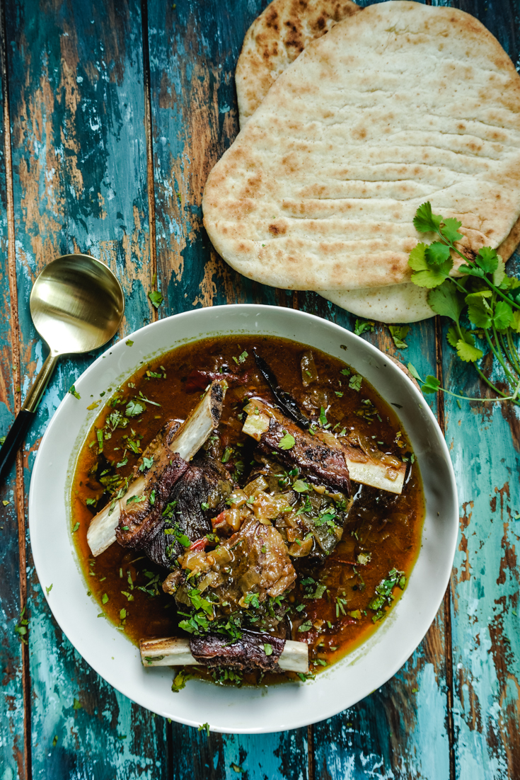 Short ribs curry in a bowl with two naans on the side