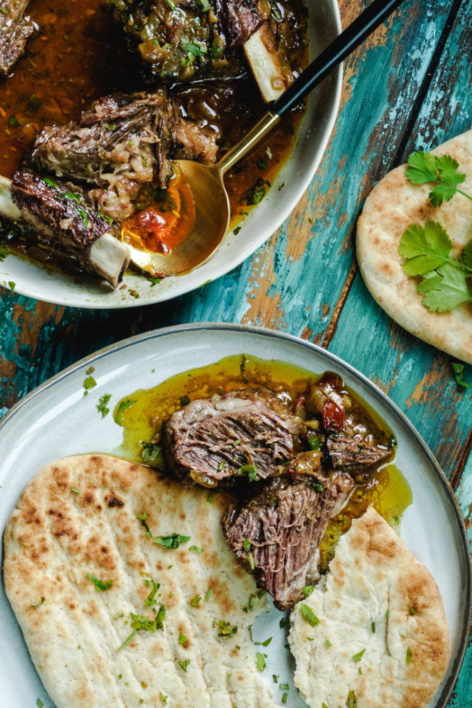 Torn naan with short ribs curry next to it on a plate