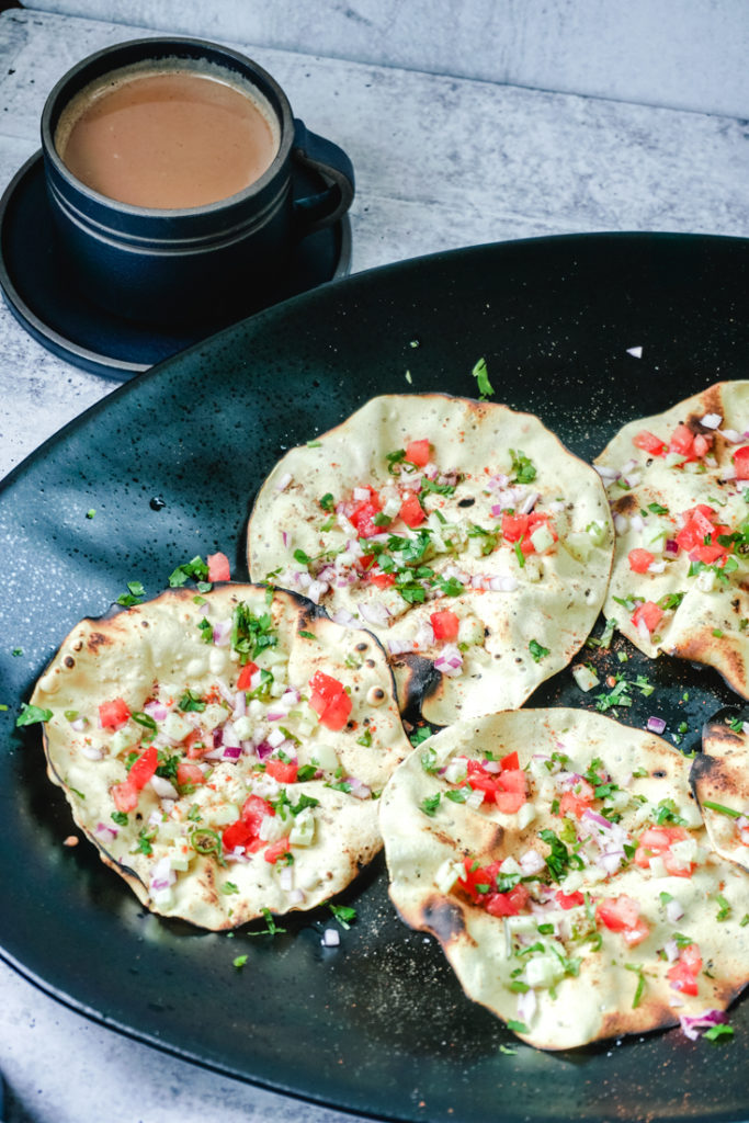 Masala papads placed in a large black platter with a black up of chai next to it