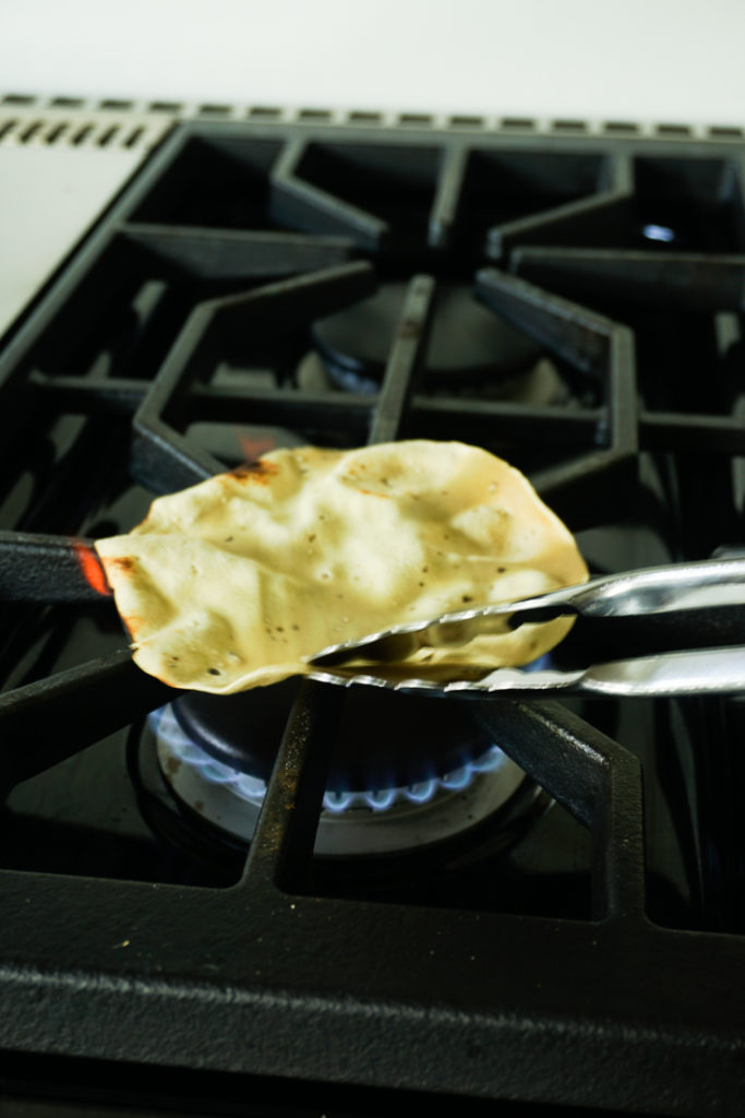 Papad held with a pair of tongs roasting on an open flame of a gas stove