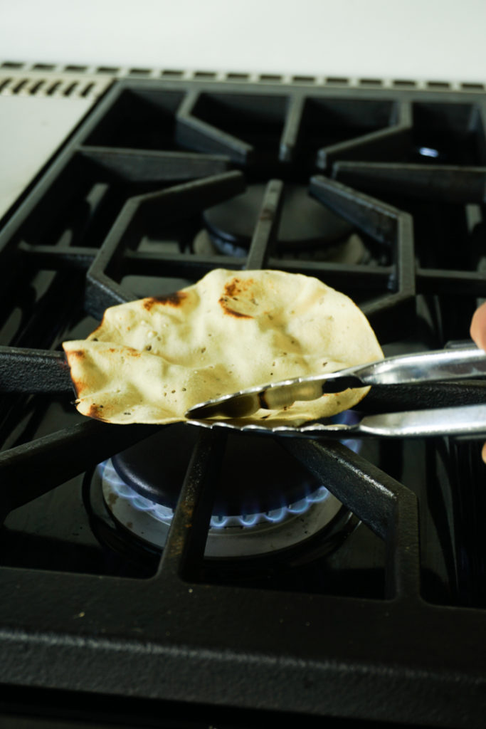 Papad held with a pair of tongs roasting on an open flame of a gas stove