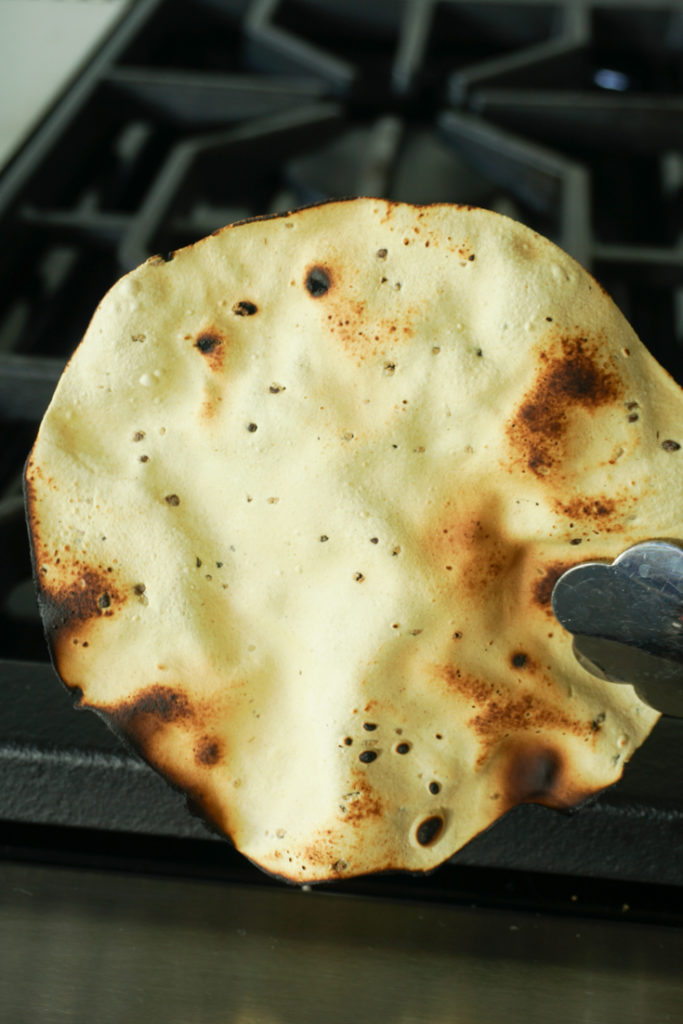 Roasted papad held with a pair of tongs to show what it should look like