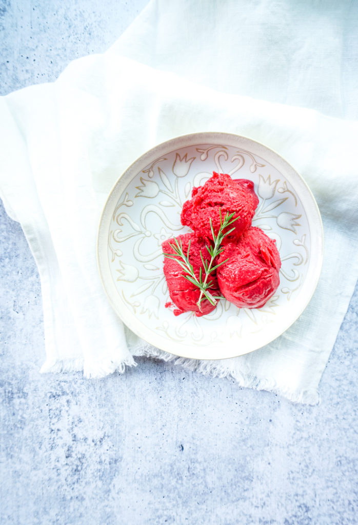Top shot of a plate with three scoops of raspberry sorbet topped with two sprigs of rosemary