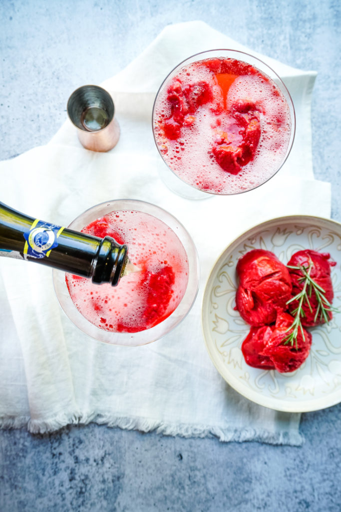 Sparkling wine being poured into a coupe glass with raspberry sorbet in it