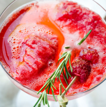 Close up shot of bright red raspberry mimosa in a champagne coupe glass