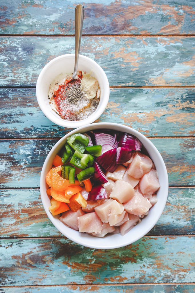 Cubed Chicken and Veggies in a white bowl and another small white bowl with spices in it