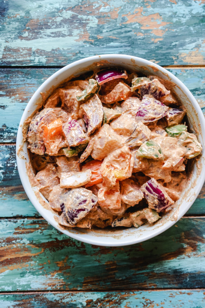 Spices and yogurt mixed with chicken and vegetables in a white bowl