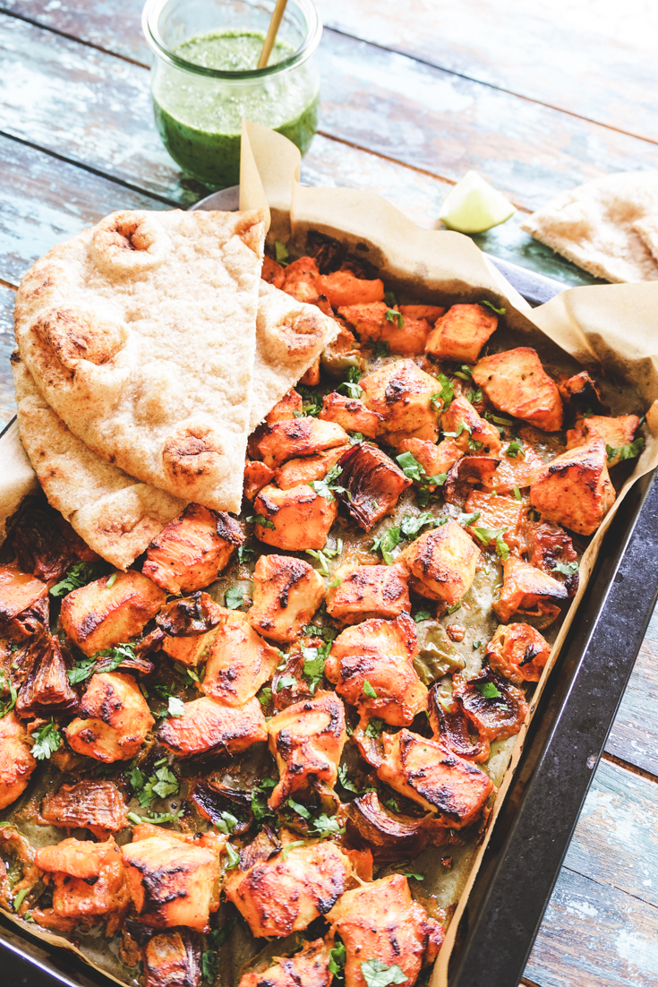 Angle shot of sheet pan with chicken tikka and two naans placed on top of it