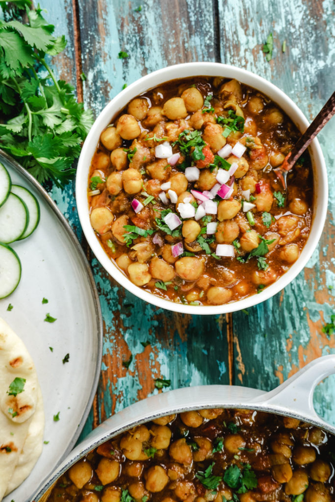 Chana Masala in a white bowl with some naan on a plate next to it