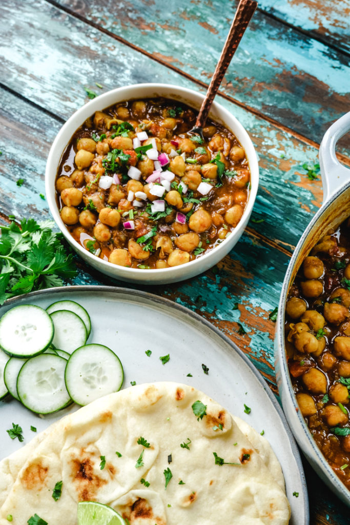 Chana Masala in a white bowl with some naan on a plate next to it
