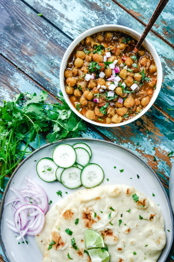 Chana Masala in a white bowl with some naan on a plate next to it