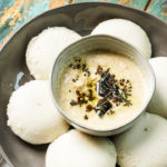 Coconut Chutney in a bowl placed inside a plate of idlis.