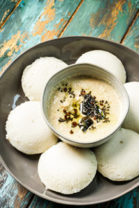 Coconut Chutney in a bowl placed inside a plate of idlis.